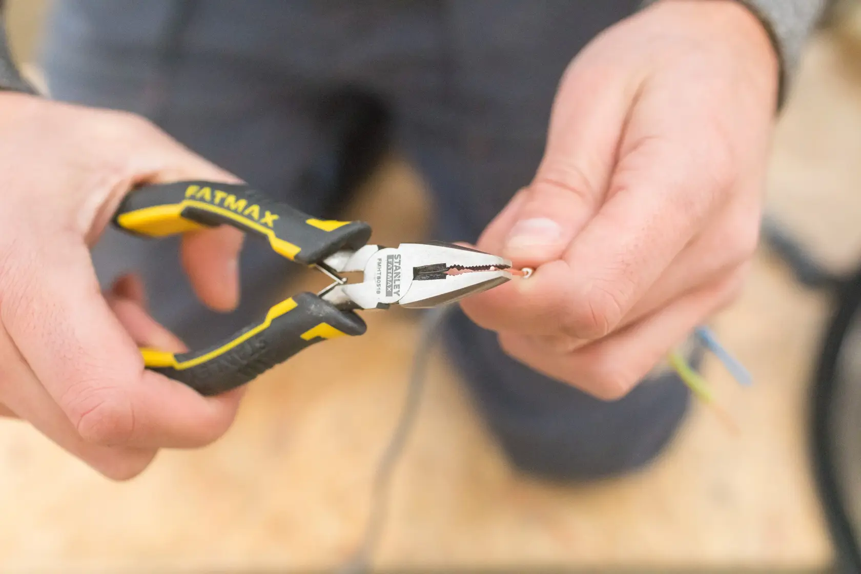 STANLEY FMHT0-80516 pliers held by hand, gripping a wire, black and yellow handle, close-up photo.