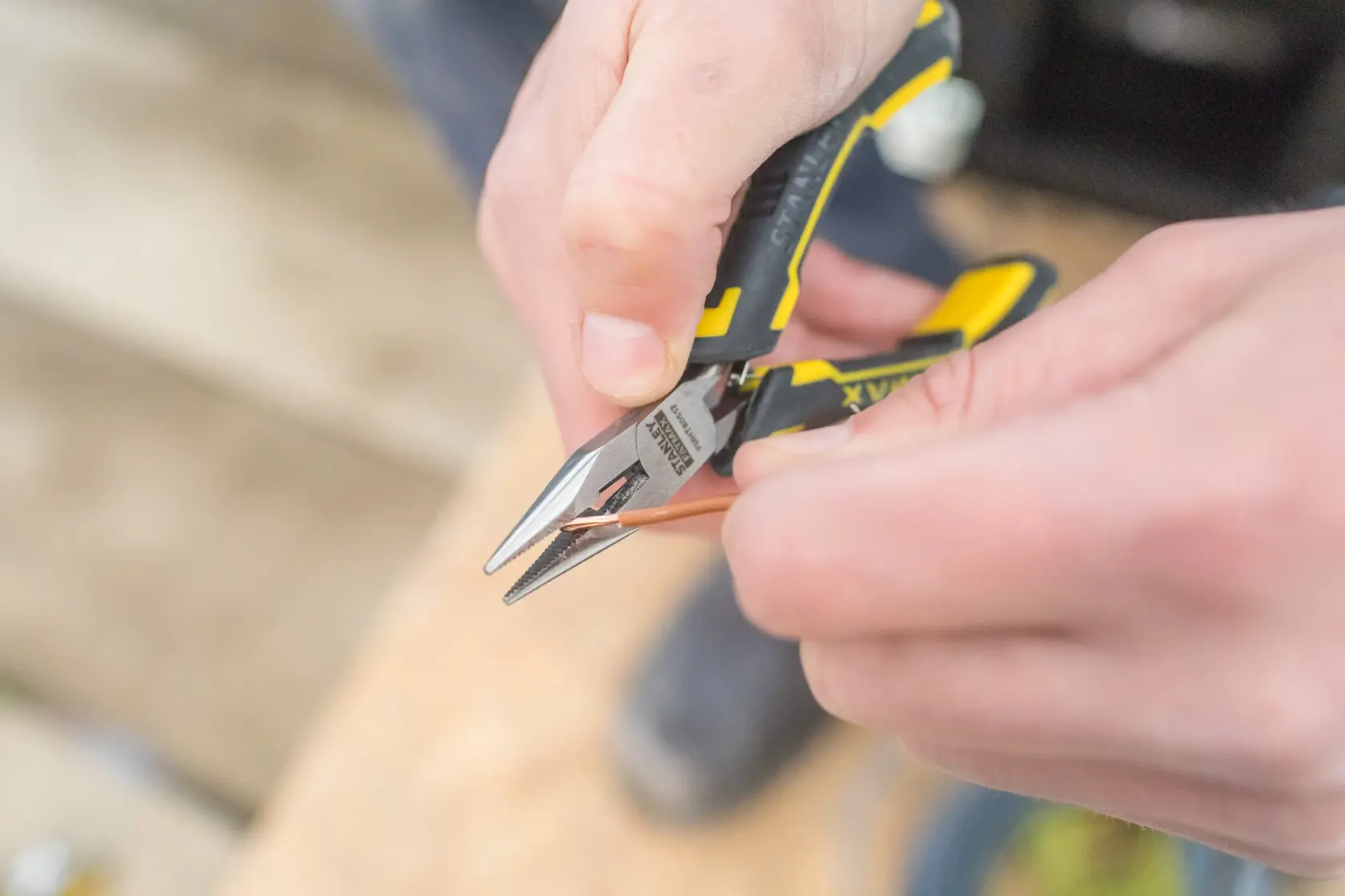 Stanley FMHT0-80517 pliers with yellow and black handle cutting copper wire, close-up photo.