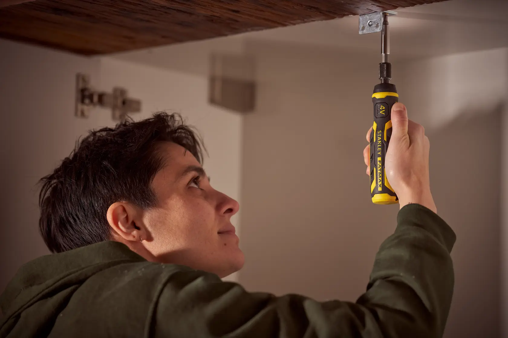 Personne utilisant le tournevis STANLEY FMHT66719-0 pour visser sous une étagère en bois en intérieur.