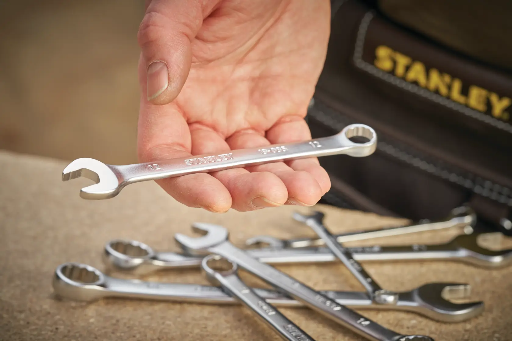 STANLEY FMMT13038-0 combination wrench held in hand, with additional wrenches on a workbench.