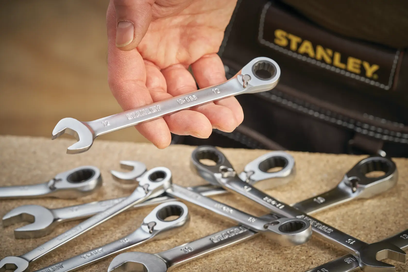 STANLEY FMMT13084-0 ratcheting wrench held in hand, with several wrenches on workbench, photography close-up.