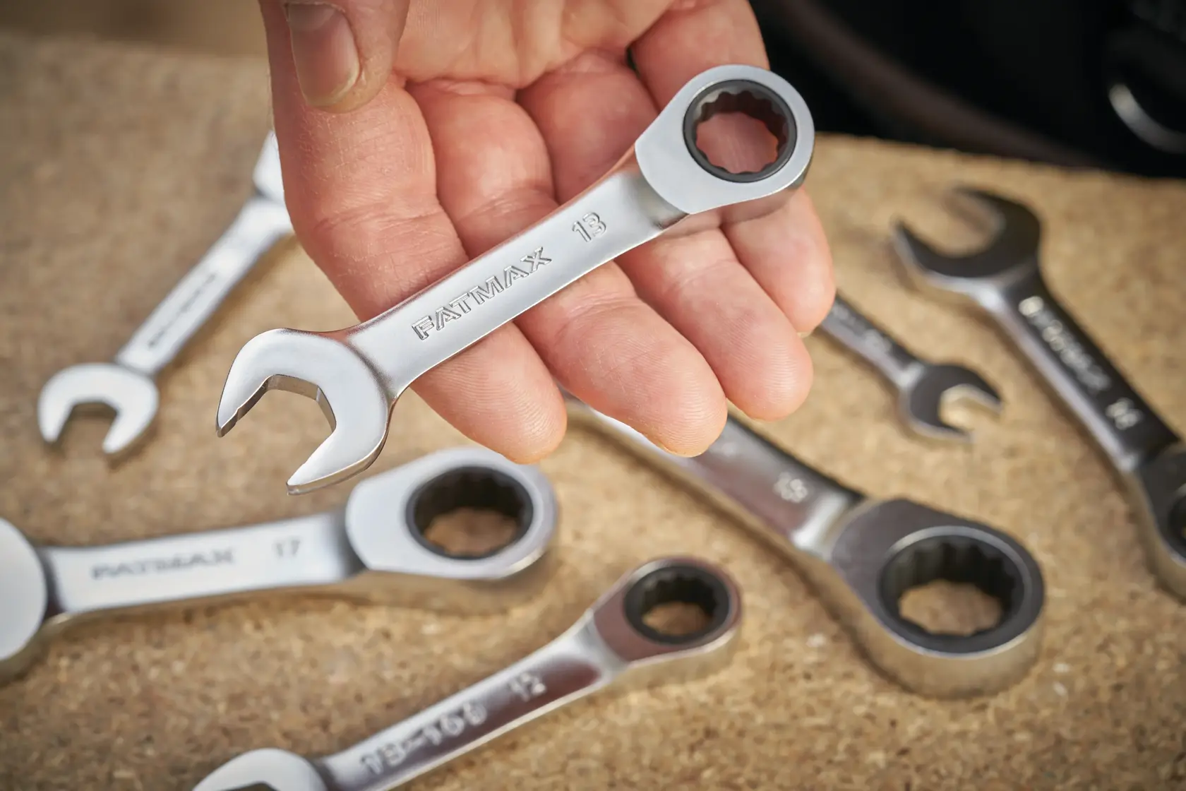 STANLEY FMMT13097-0 ratcheting combination wrench held in hand, with other wrenches on a work surface.