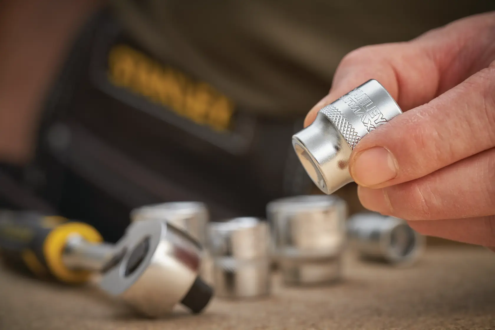 STANLEY FMMT17220-0 socket set photography, close-up of hand holding silver socket with ratchet tool.