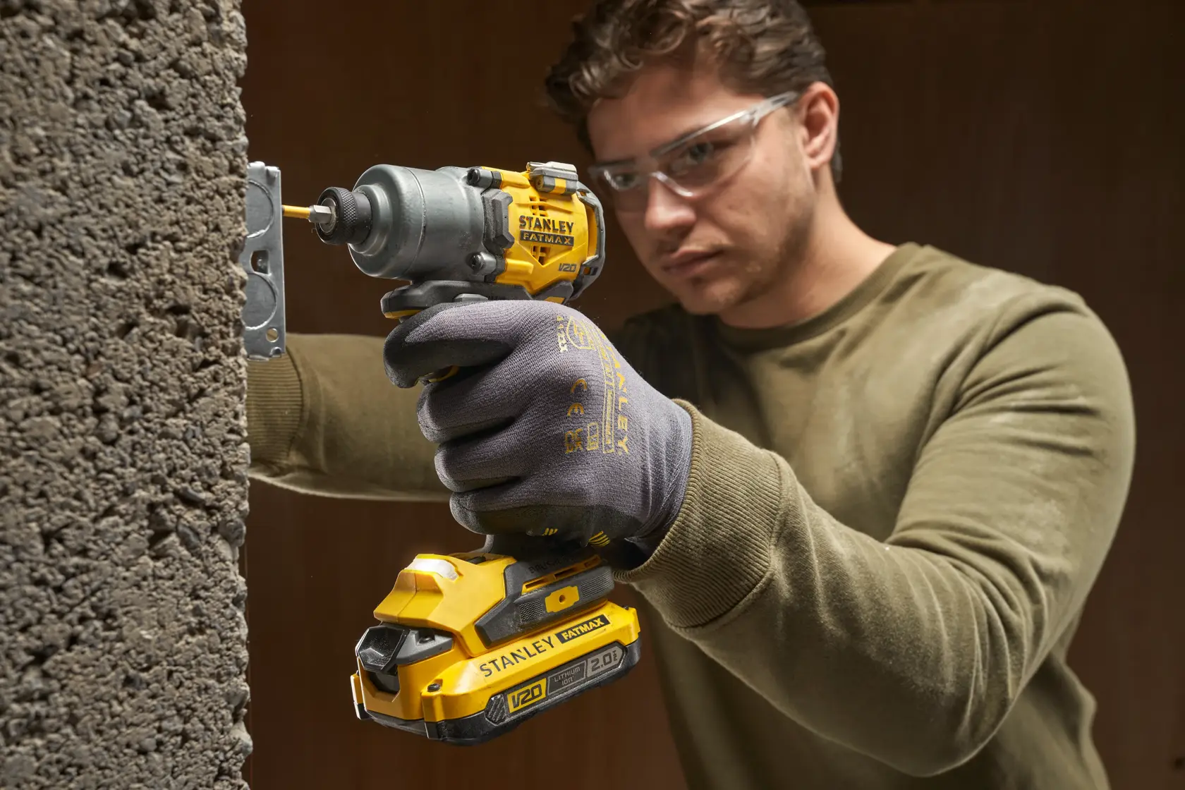 Foto eines Arbeiters mit STANLEY SFMCF830D2K Akku-Schlagschrauber in Gelb und Schwarz an einer Betonwand.