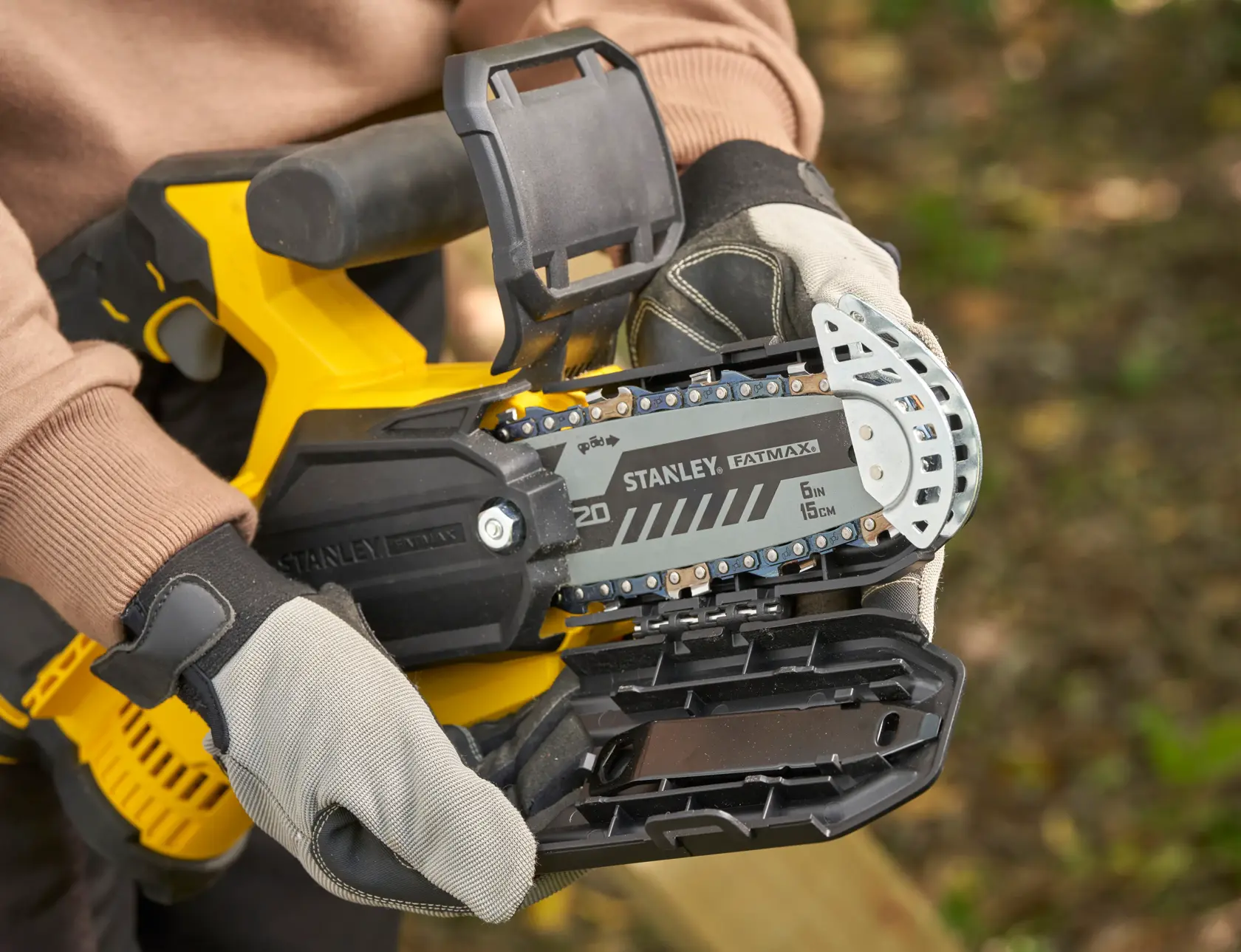 STANLEY SFMCPS415D1 FatMax tronçonneuse en gros plan, guide-chaîne et gants de protection en extérieur.