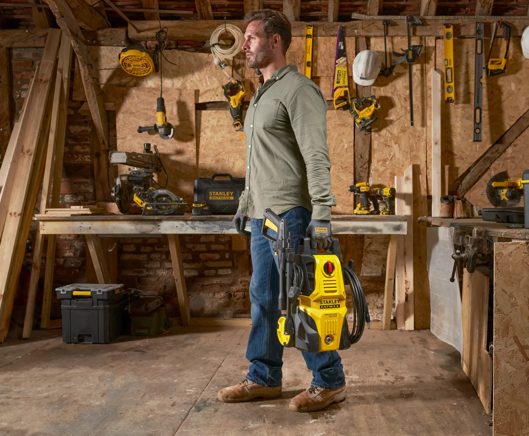 Stanley SFMPW1740 Hochdruckreiniger, von einer Person in Werkstatt mit Holzwerkzeugen gehalten.