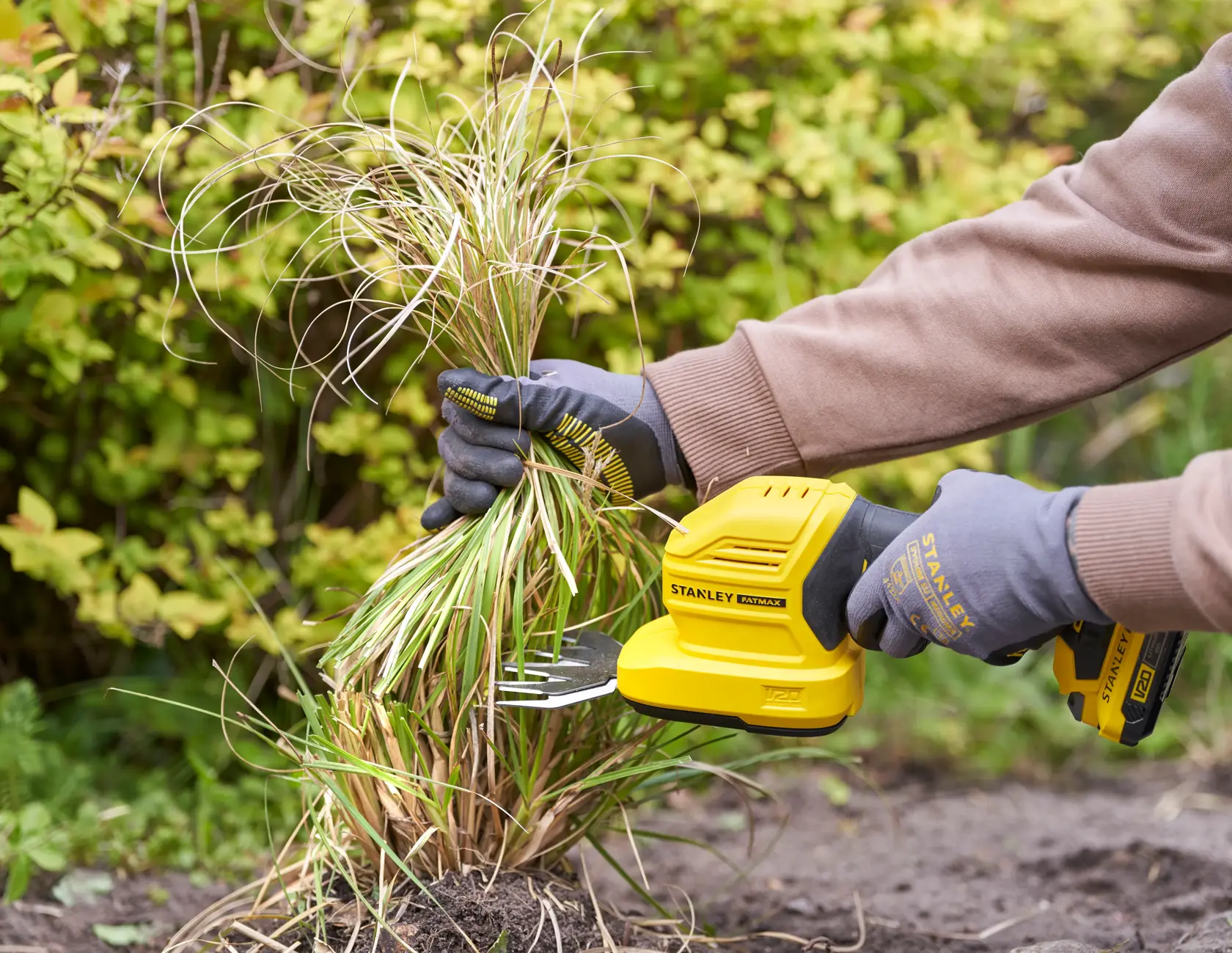 Foto der STANLEY STCSS20B Grasschere im Einsatz, gelbes Werkzeug wird von behandschuhten Händen zum Rasenschneiden genutzt.