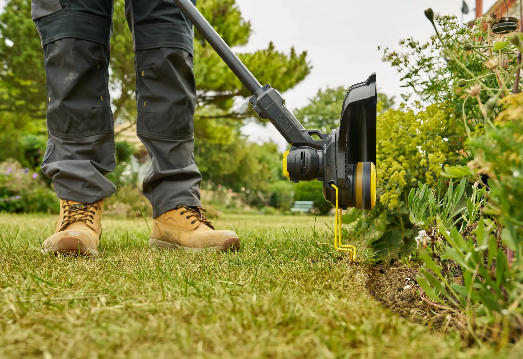 STANLEY STCST933B Rasentrimmer im Einsatz am Rasenrand, Seitenansicht aus der Nähe, Trimmen am Blumenbeet.
