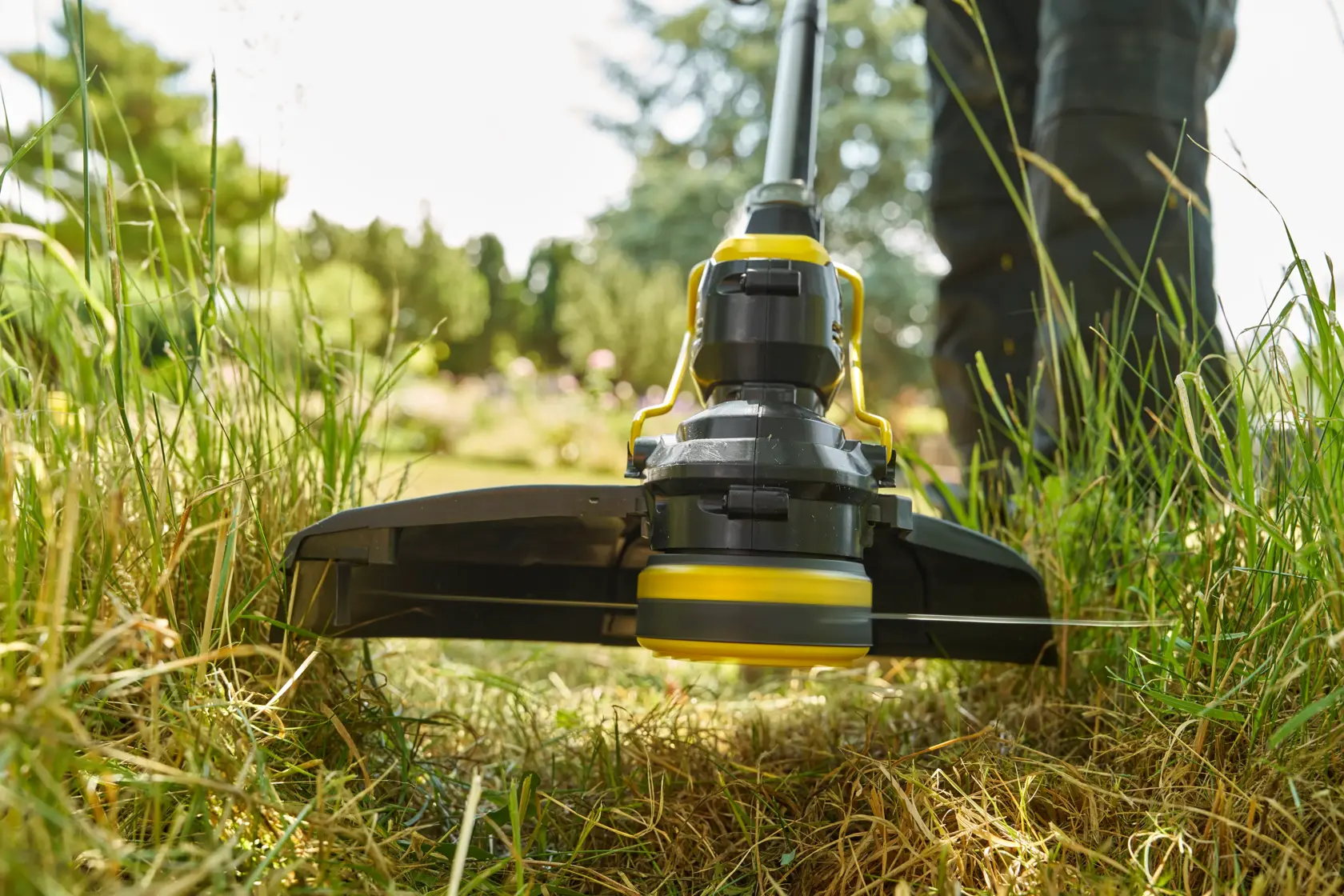 STANLEY STCST933B Rasentrimmer in Betrieb, Nahaufnahme aus niedriger Perspektive der Schneidkopf trimmt hohes Gras im Freien.