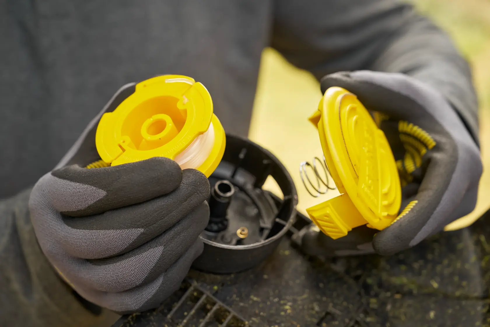 STANLEY STCST933B assemblage de bobine de coupe-bordures, photo gros plan de la bobine jaune et du couvercle dans des mains gantées.