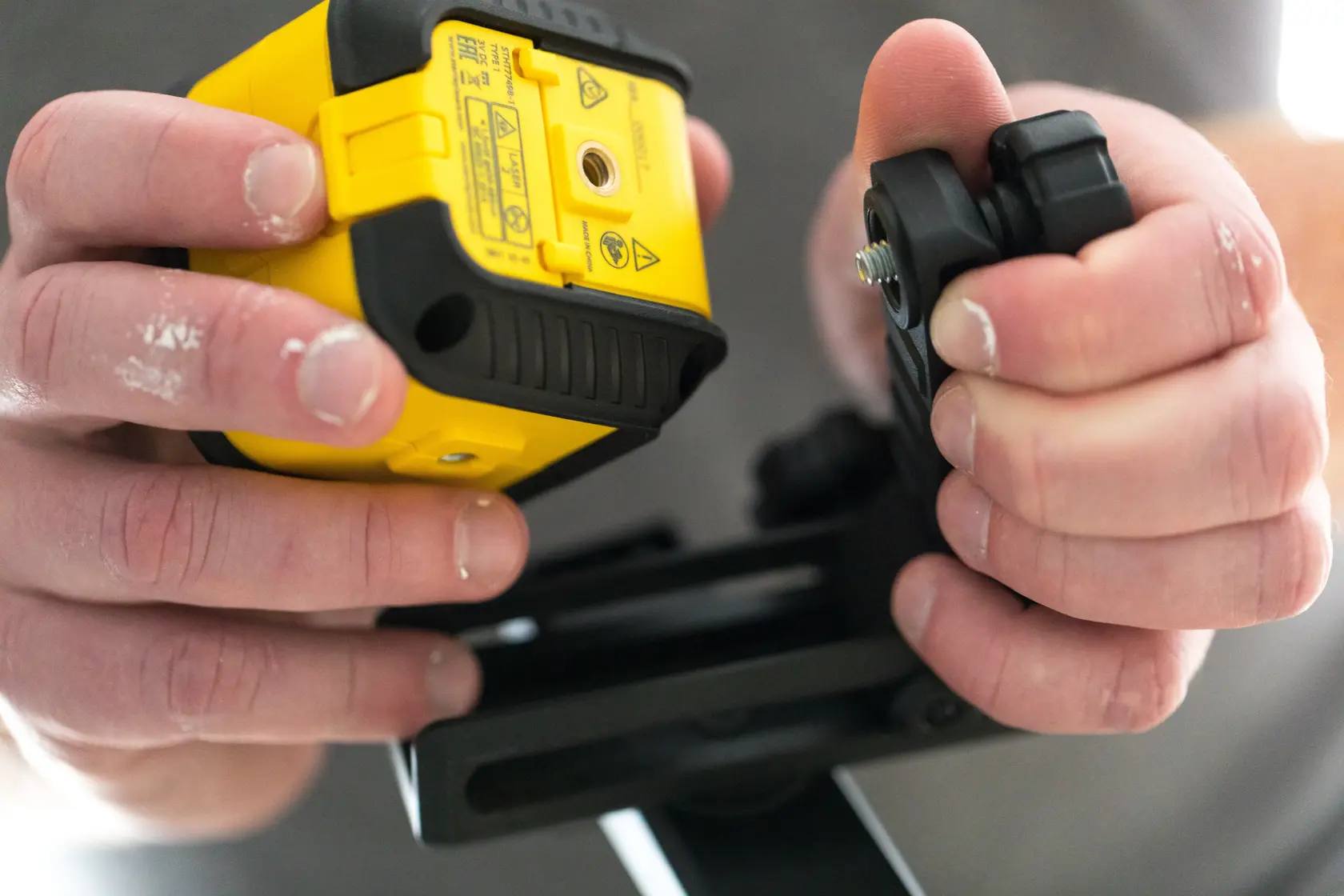 Stanley STHT77499-1 Fotografie einer Hand, die einen Laser-Nivellierer und eine Montagehalterung aus der Nähe hält.