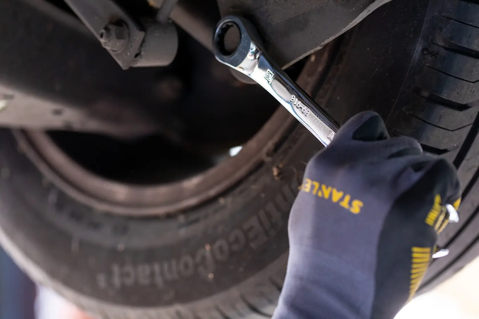 STANLEY STMT89915-0 ratcheting wrench used on car wheel, close-up with gloved hand.