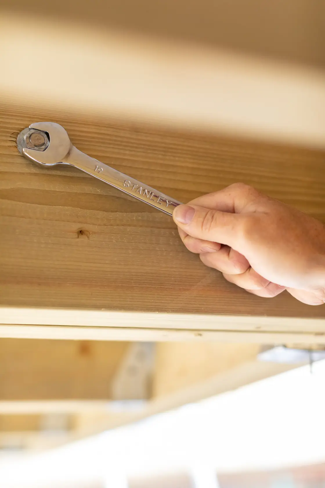 STANLEY STMT89915-0 wrench in use tightening a bolt on wood, close-up photography.