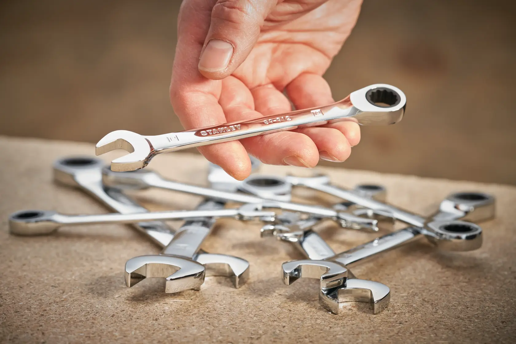 STANLEY STMT89918-0 ratcheting combination wrench set, one wrench held in hand, others on wooden surface.