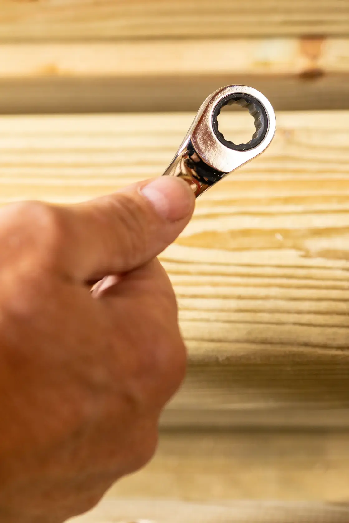 STANLEY STMT89918-0 ratcheting wrench held in hand, close-up against wooden planks, photography category.