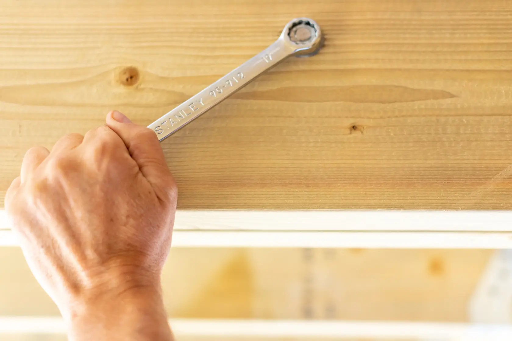 Photo of STANLEY STMT95792-0 ratcheting wrench in hand tightening bolt on wooden surface.